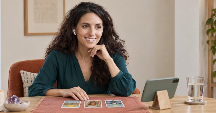Tarot reader listening through an earpiece with cards and amethyst on a round table.